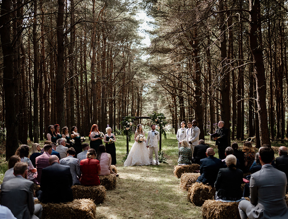 Woodland ceremony with guests sitting on bales of hay